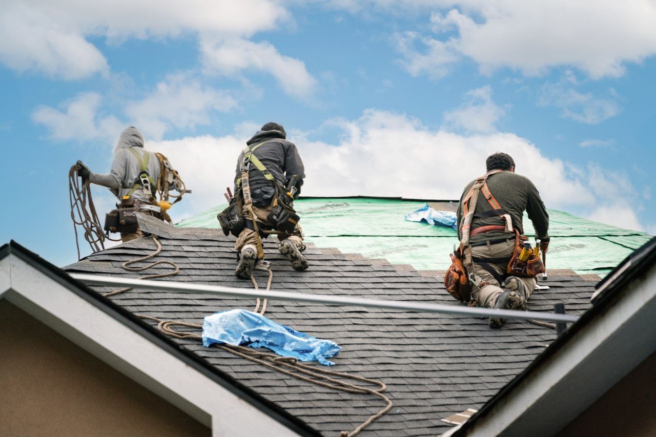 Emergency roof repair crew applying protective weather tarping to stop an active leak.